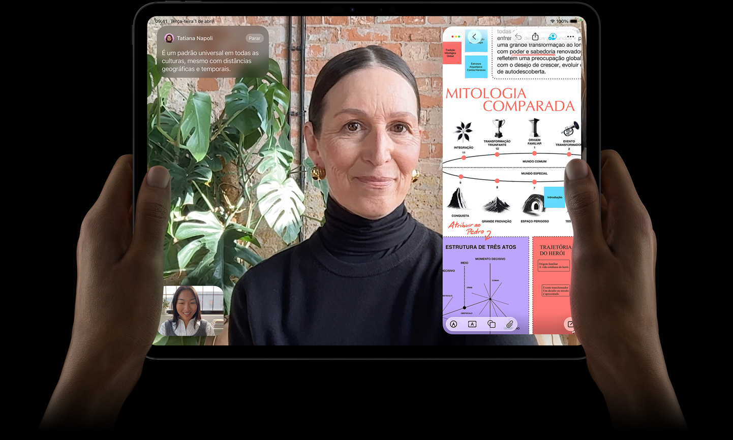Parte da frente do iPad Pro preto-espacial, com as mãos esquerda e direita segurando o aparelho na horizontal, tela com borda preta mostrando uma conversa no FaceTime sendo traduzida ao vivo e um app educativo mostrando uma apresentação sobre Mitologia Comparada com textos, diagramas e anotações manuscritas