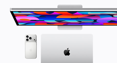 An Apple Display behind an iPhone 17 Pro in Silver color and a closed MacBook in Silver color