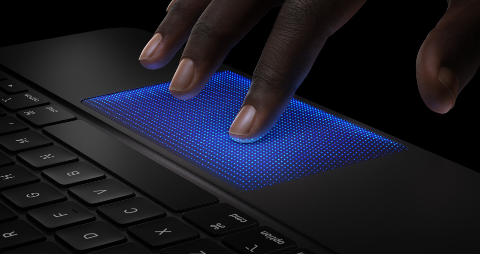 Animation d’une main qui survole le pavé tactile d’un Magic Keyboard, l’index et un éclat bleu montrent l’action du toucher pour illustrer la rétroaction haptique